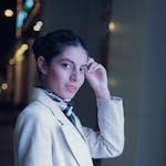 Portrait of a stylish woman in a light suit and scarf, posing outdoors at night in Dubai.