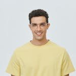 Portrait of a young man wearing glasses and a yellow shirt, smiling brightly.